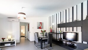A modern living room with a flat-screen TV, grey sofa, dining table, and chairs. - Villa 'Hortet' with Private Pool, Wi-Fi and Air Conditioning (Campos)