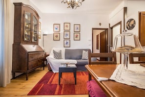 Ein Wohnzimmer mit einem Holzschrank, einer Couch, einem Couchtisch und einem Esstisch mit Glasplatte.
