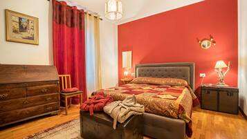 A bedroom with a bed, dresser, chair, and a small table with a lamp.