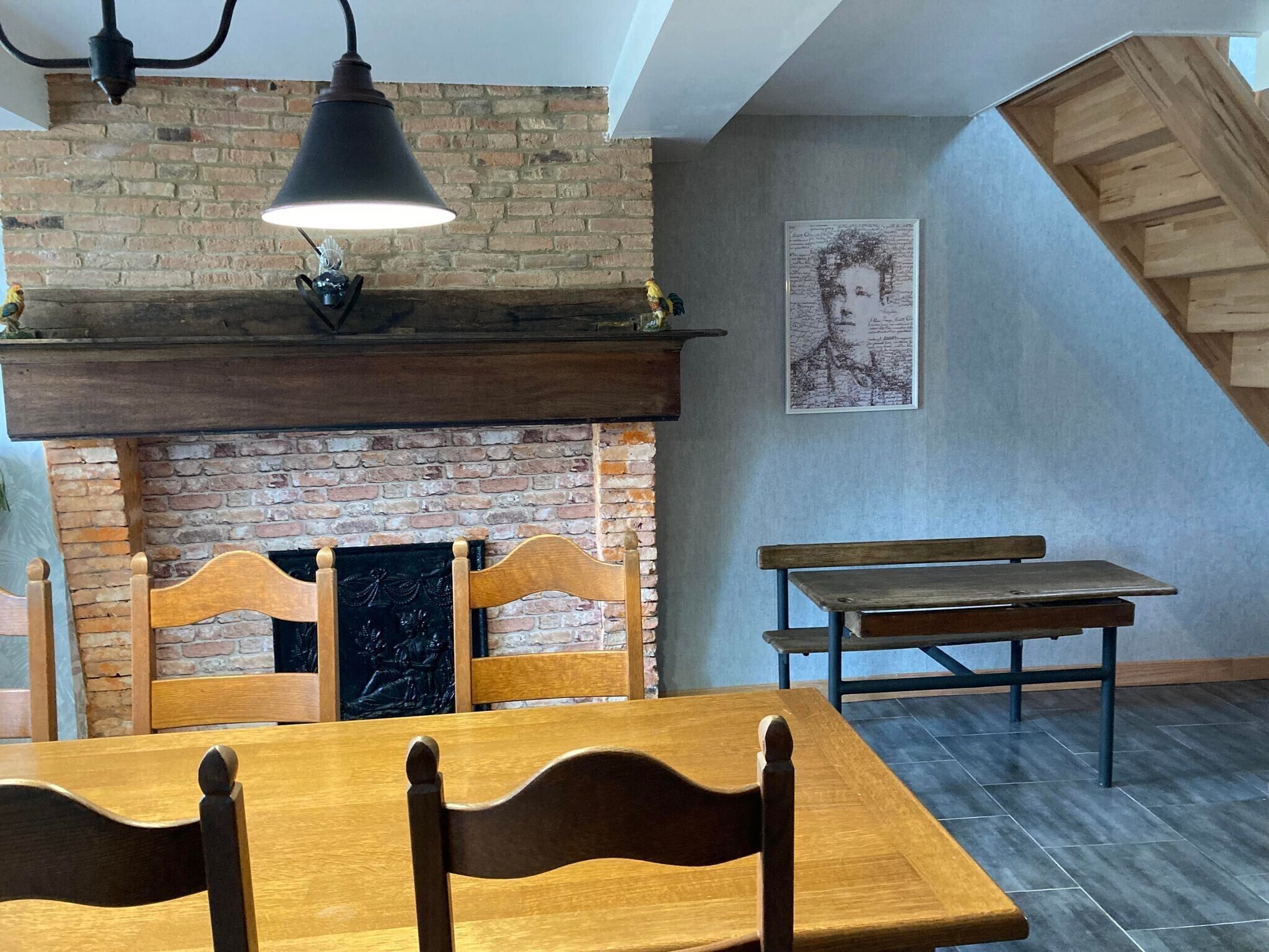 A dining area with a brick fireplace, wooden chairs, a table, and a bench.