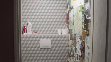 A bathroom with a toilet, a shelf with toiletries, and a wall covered with various pictures.