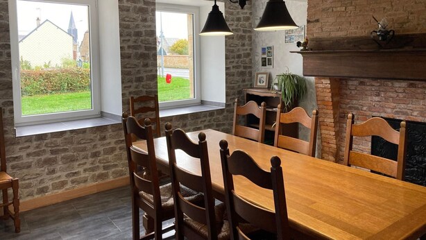 Un comedor con pared de ladrillo, dos ventanas, una chimenea y una lámpara colgante.