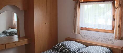 Ein Schlafzimmer mit einem Bett, einem Holzschrank, einem Fenster mit Vorhängen und einer Wanddekoration.