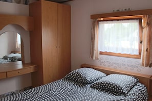 Un dormitorio con cama, un armario de madera, una ventana con cortinas y un adorno en la pared.