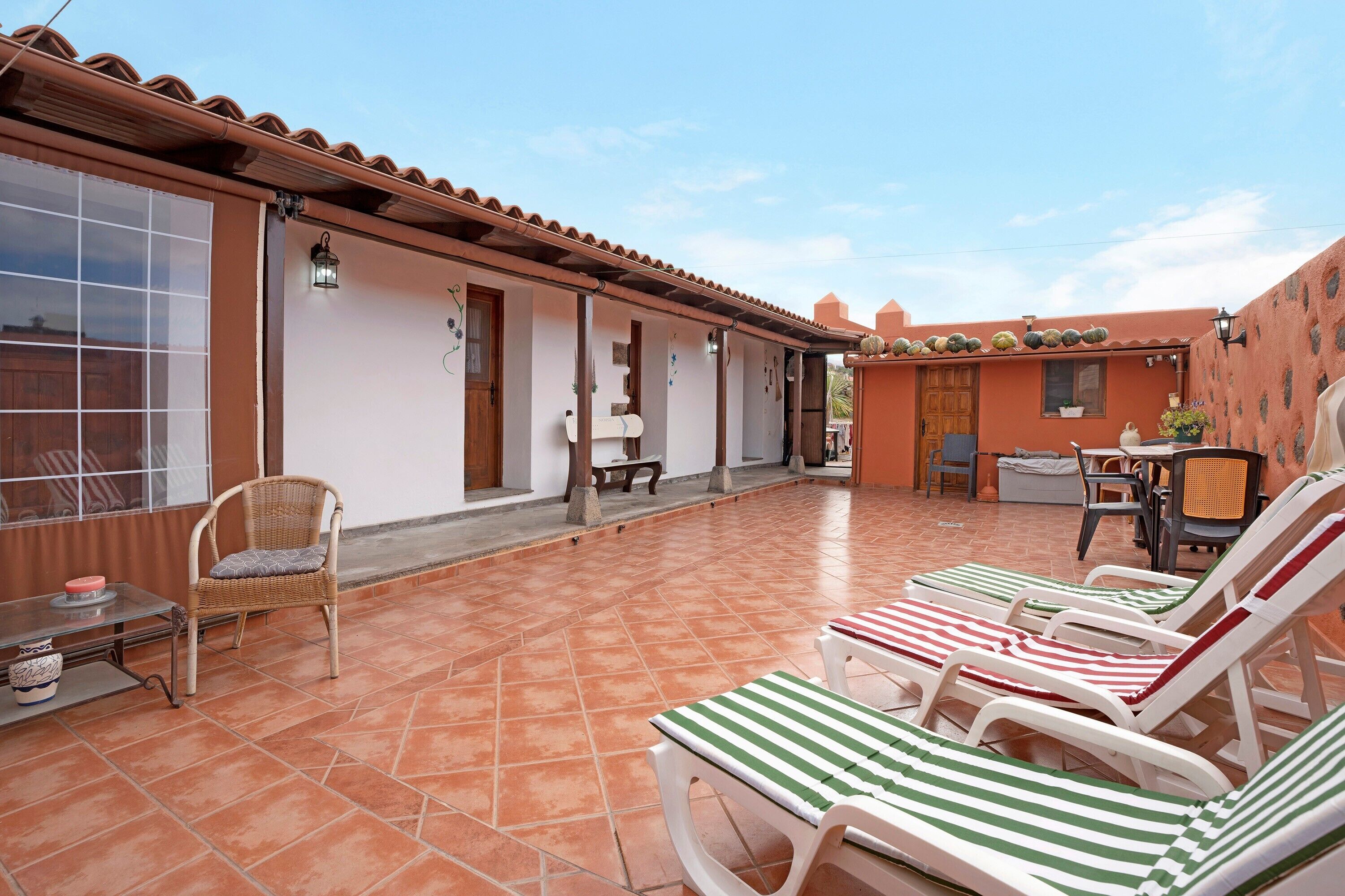A covered patio with tiled flooring, wicker chairs, and striped lounge chairs.