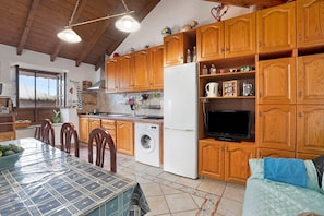 A kitchen with wooden cabinets, a washing machine, a refrigerator, and a dining table with chairs.