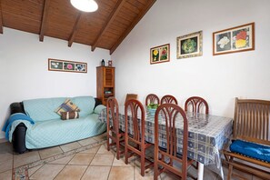 A dining area with a table set for four, surrounded by wooden chairs, a sofa, and a wooden cabinet.