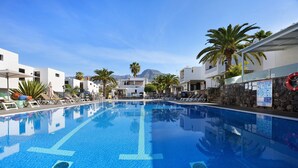 Una piscina con agua cristalina azul, rodeada de edificios blancos y palmeras.