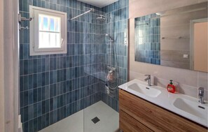 A bathroom with blue tiles, a shower, a sink, a mirror, and a window.