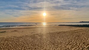 Una playa con atardecer, orilla arenosa y mar tranquilo.