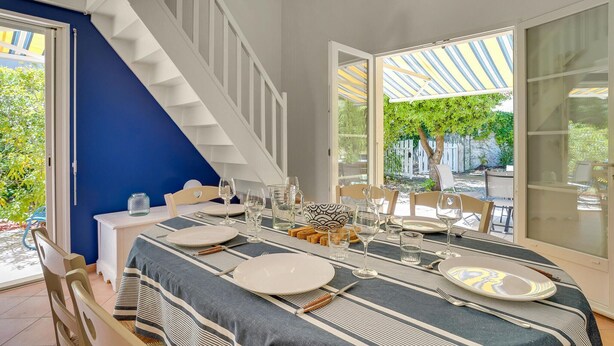 Un comedor con una mesa preparada para cuatro personas, una escalera y vistas al exterior.