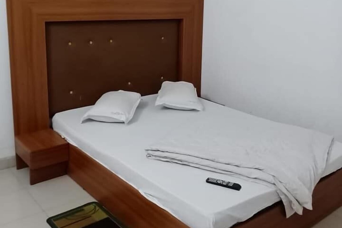 A single bed with a wooden headboard, white bedding, and a remote control on the bed.