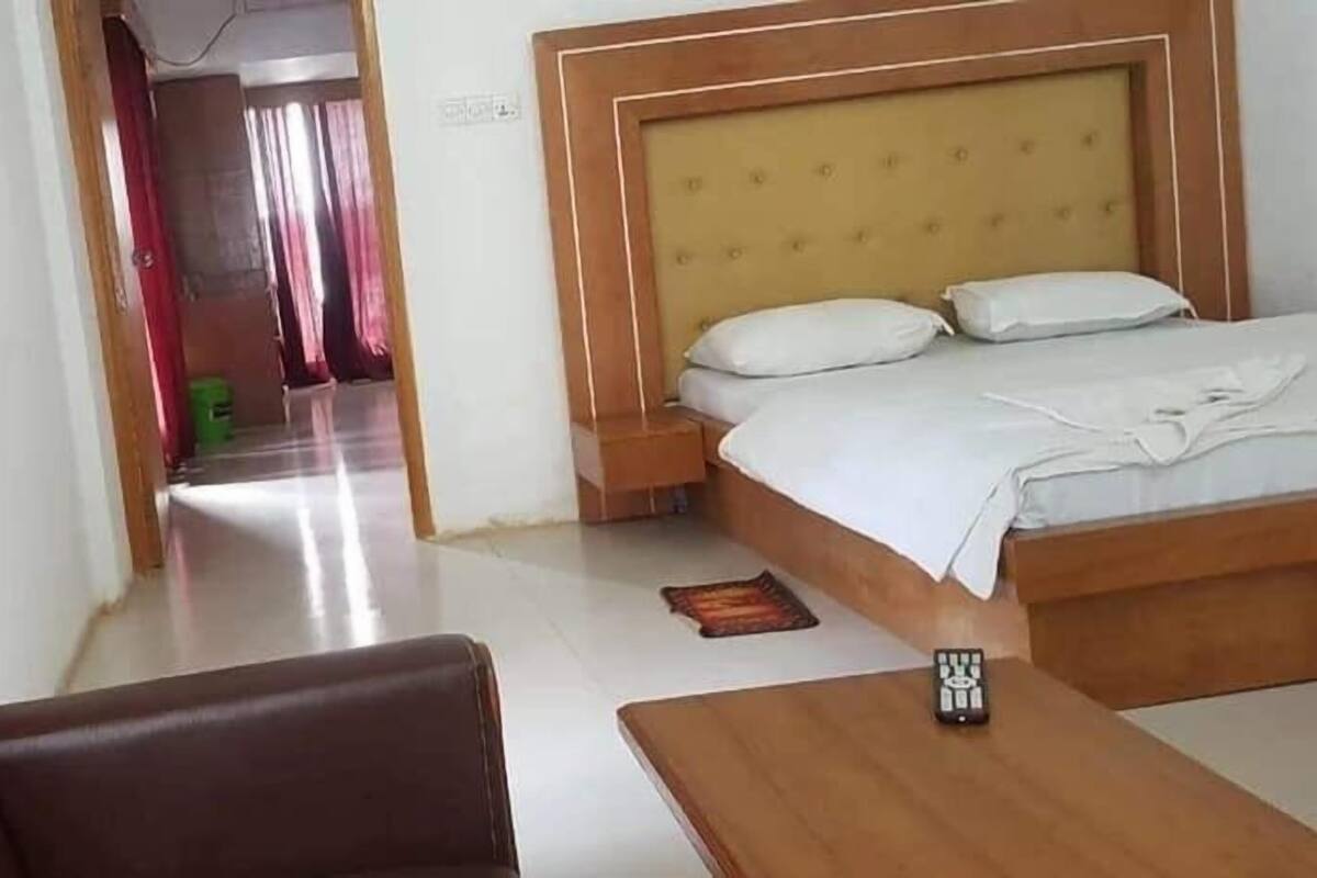 A hotel room with a bed, a wooden headboard, a small table, and a remote control on the table.