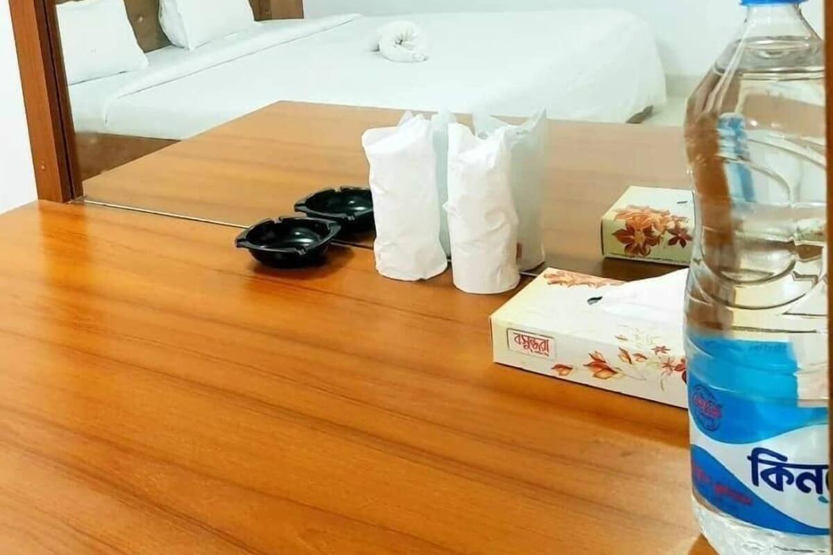 A hotel room with a wooden bed, white bedding, a bedside table with toiletries, and a water bottle.