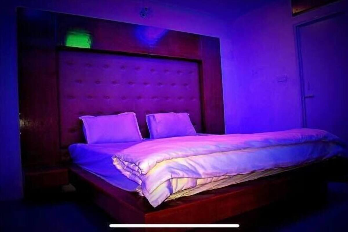 A bed with a wooden headboard and two pillows in a room with purple lighting.
