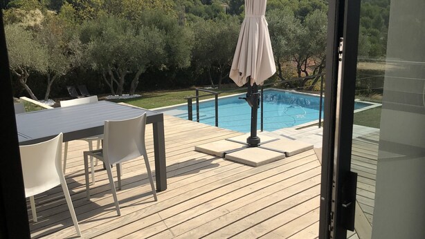 Une terrasse en bois avec une table et des chaises, une piscine et une vue sur un paysage montagneux.