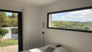 Une chambre avec une grande fenêtre, un lit, une lampe de chevet et une petite table avec une lampe.