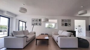 Un salon moderne avec deux canapés blancs, une table basse en bois et une grande fenêtre qui laisse entrer la lumière naturelle.