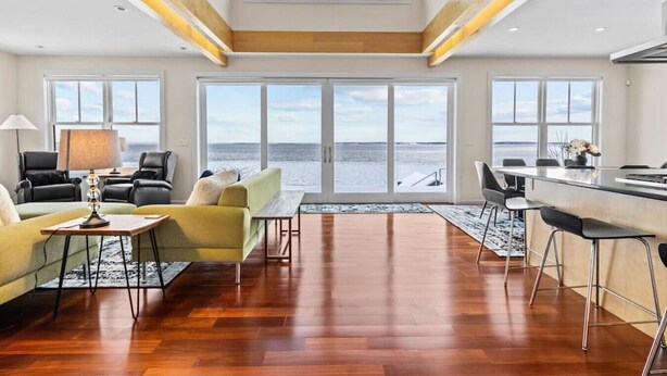 A spacious living area with a large window overlooking the sea, wooden flooring, and modern furniture. - Chic Modern Lake Getaway! (Colchester)