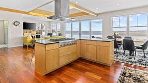 A modern kitchen with wooden cabinets, a central island, and a large window overlooking a scenic view. - Chic Modern Lake Getaway! (Colchester)