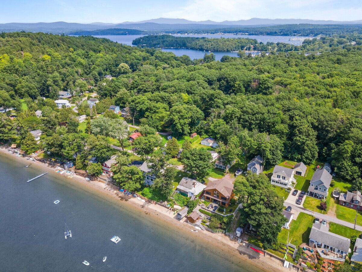 An aerial view of a coastal residential area with houses, a beach, and a lake.