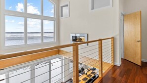 A spacious room with a large window overlooking a beach, a wooden staircase, and a fireplace. - Chic Modern Lake Getaway! (Colchester)