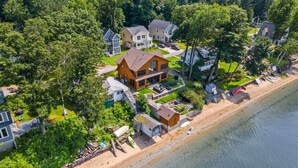 An aerial view of a coastal property with multiple houses, a beach, and a forested area. - Chic Modern Lake Getaway! (Colchester)