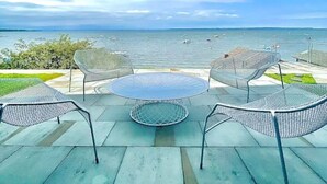 An outdoor seating area with a round table and chairs, overlooking a body of water with boats. - Chic Modern Lake Getaway! (Colchester)