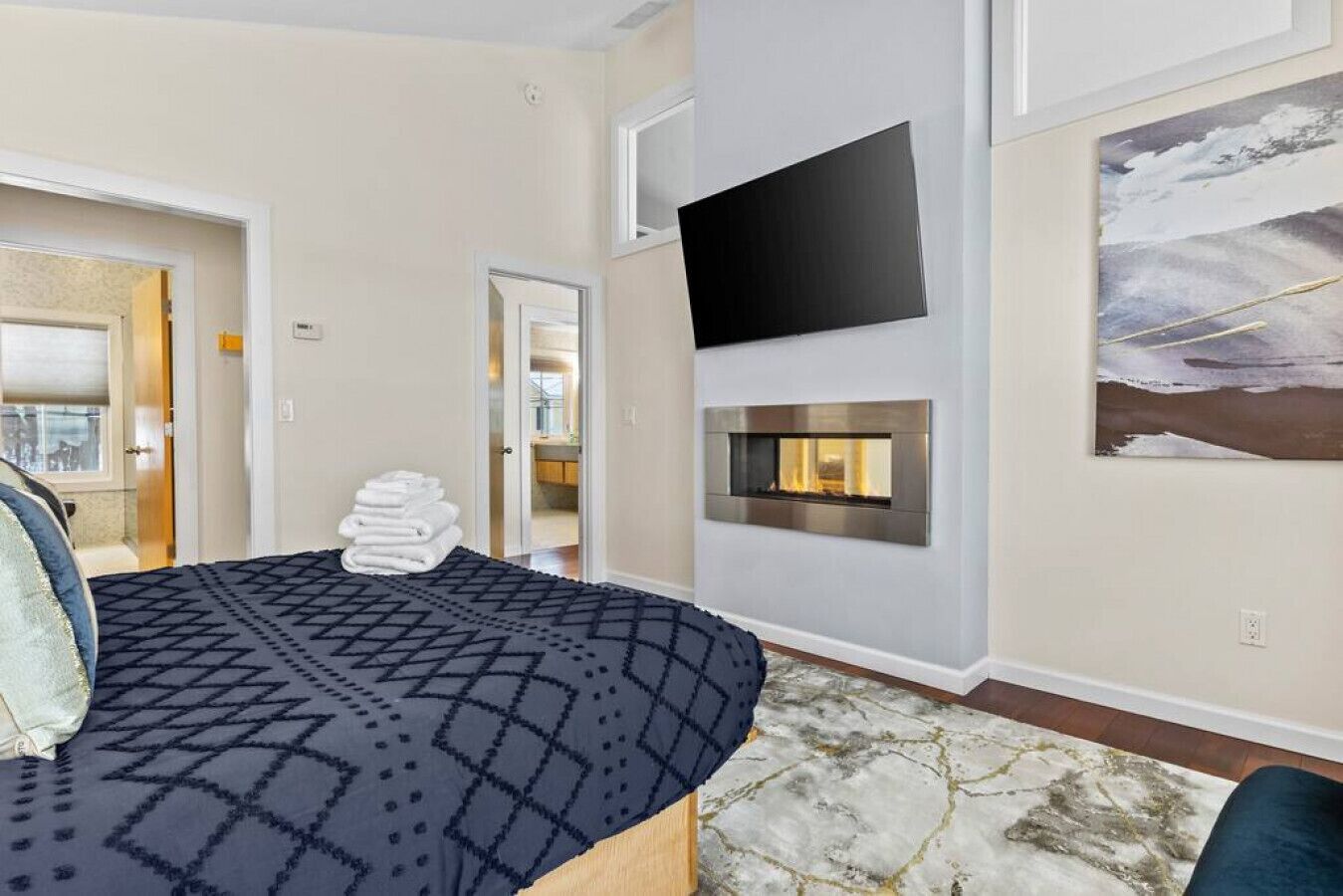 Una habitación de hotel moderna con una cama, una chimenea, un televisor montado y un cuadro en la pared.