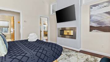 Una habitación de hotel moderna con una cama, una chimenea, un televisor montado y un cuadro en la pared.