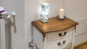 Um quarto com uma mesa de cabeceira de madeira, uma vela branca e um abajur mosaico.