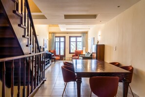 A spacious living area with a large wooden dining table, several chairs, a piano, and a staircase. - George's Poet Maisonette (Rethymno)