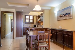 A spacious kitchen with wooden cabinets, a dining area with a large table and chairs, and a painting on the wall. - George's Poet Maisonette (Rethymno)