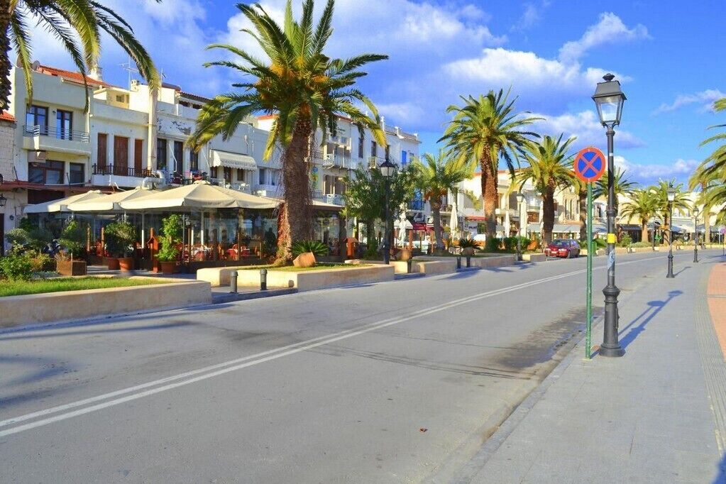 Eine Straße gesäumt von Palmen und Gebäuden, mit blauem Himmel und einem blauen Schild.