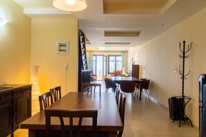 A spacious dining area with a long wooden table and chairs, a coat rack, and a view of the outdoors through large windows. - George's Poet Maisonette (Rethymno)