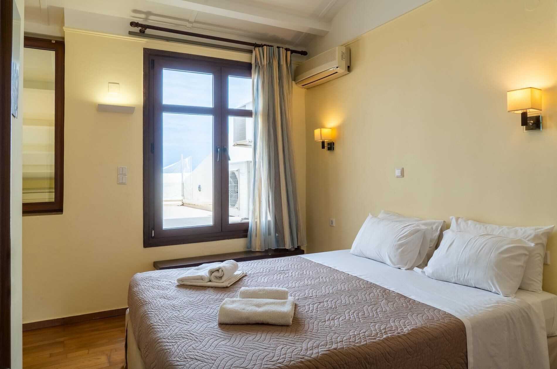 Ein Hotelzimmer mit einem Bett, zwei Wandlampen, einem Vorhangfenster und einer Klimaanlage.
