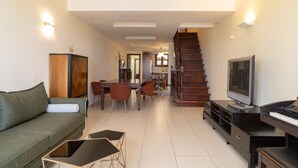 Una sala de estar con un sofá, una mesa de centro, un televisor y una escalera que sube a otro nivel.