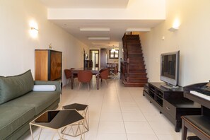 Una sala moderna con un sofá, una mesa de comedor, sillas, una escalera y un televisor.