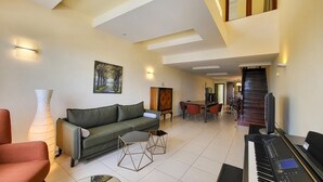 Una sala de estar moderna con un sofá verde, una zona de comedor con mesa y sillas, un piano y una escalera.