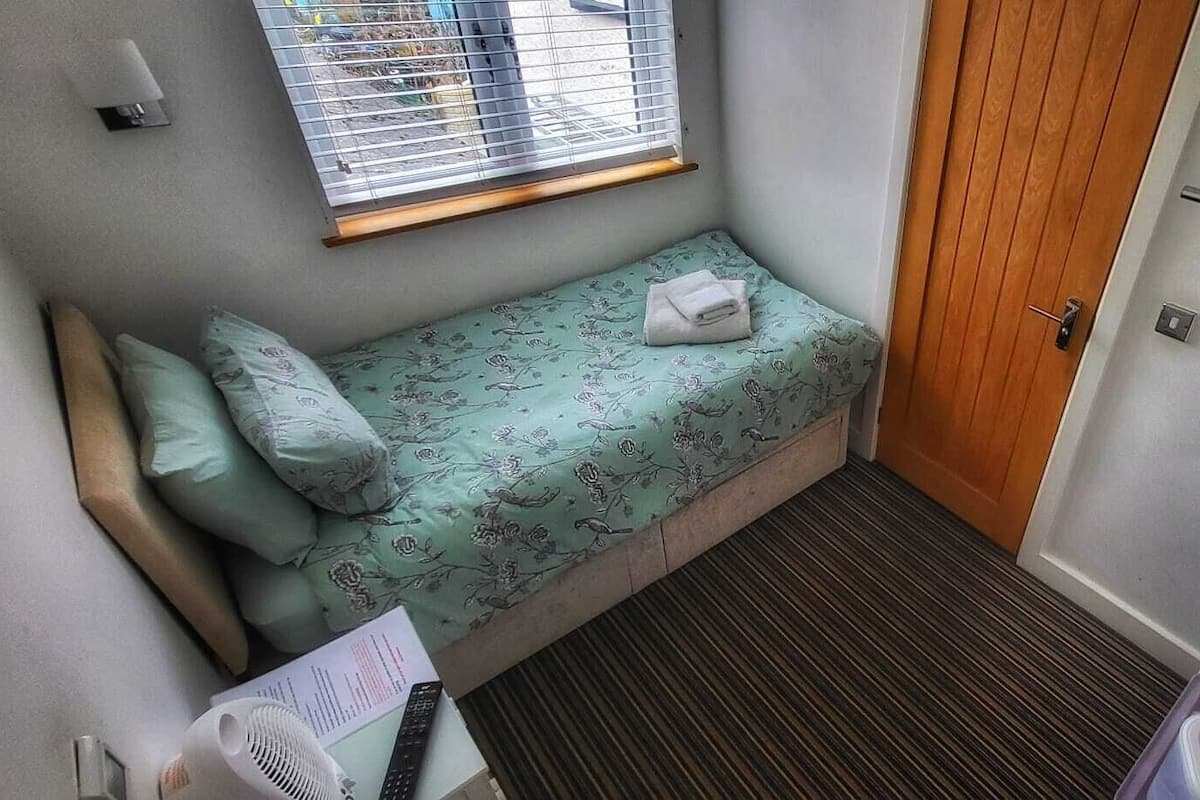 A small, narrow room with a single bed, a window, and a door.