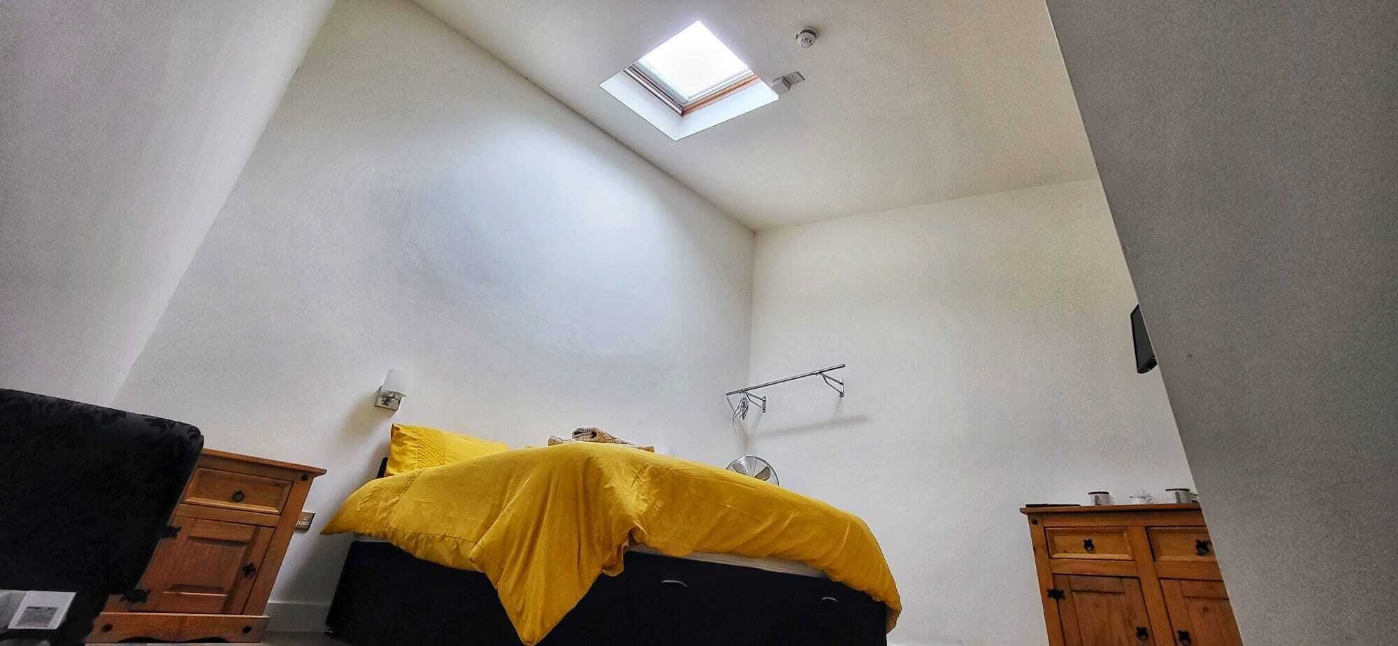 A room with a sloped ceiling, a bed with a yellow cover, wooden cabinets, and a ceiling fan.