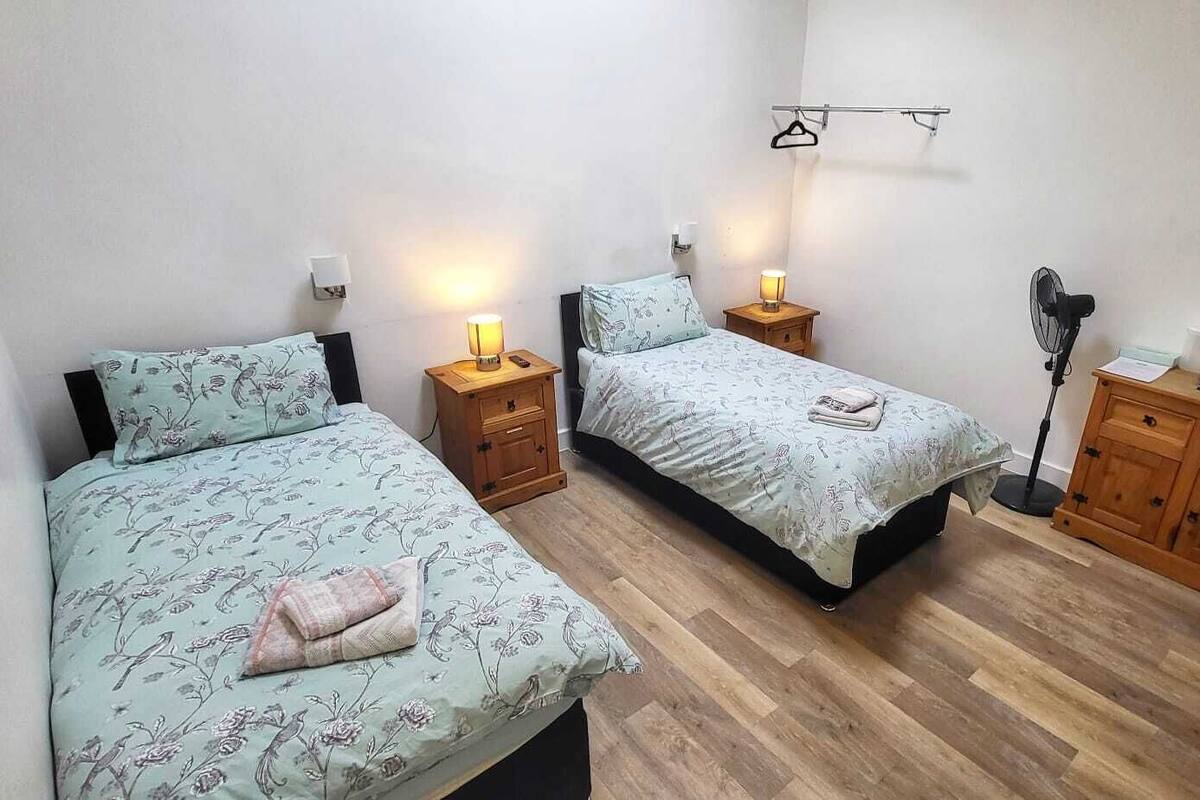 A bedroom with two single beds, wooden nightstands, a bedside table, a wardrobe, and a wall-mounted TV.