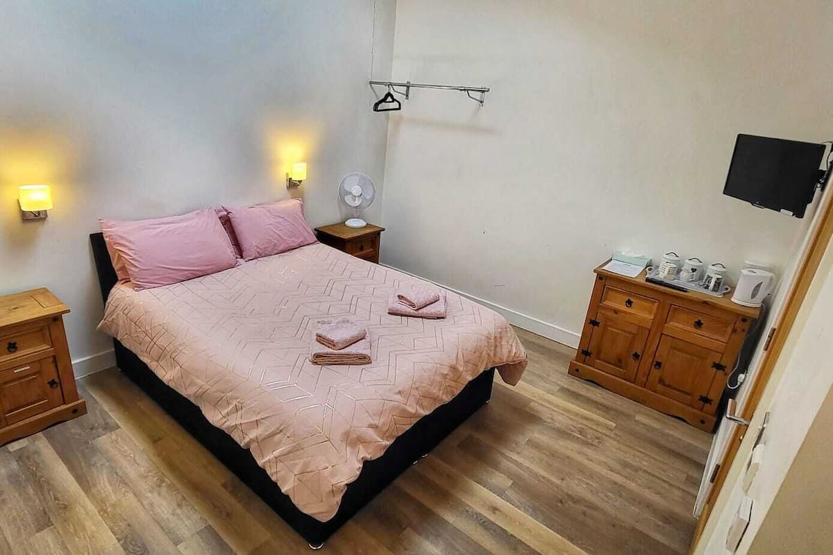 A bedroom with a bed, two bedside tables, a wooden dresser, and a wall-mounted TV.