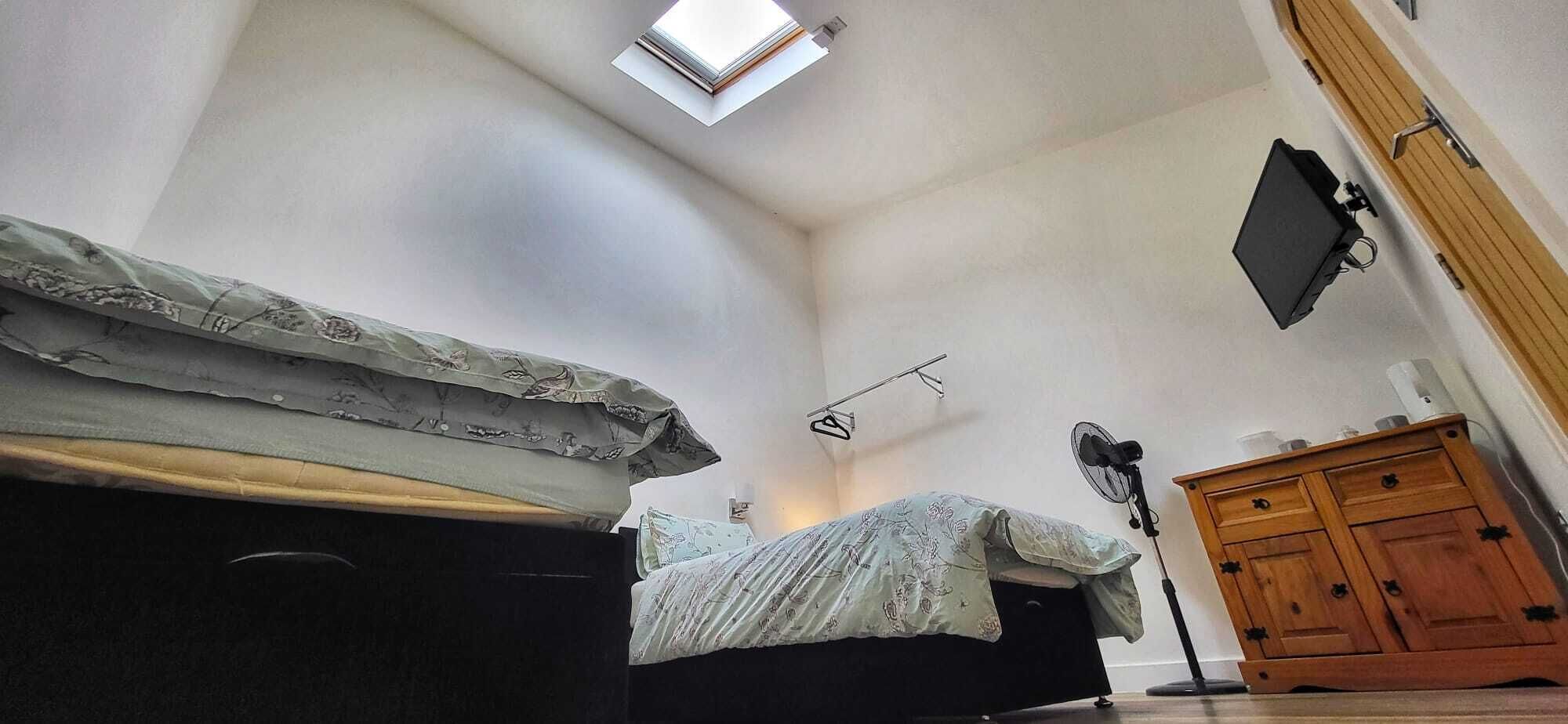 A bedroom with a bed, a wooden dresser, a ceiling fan, and a skylight.