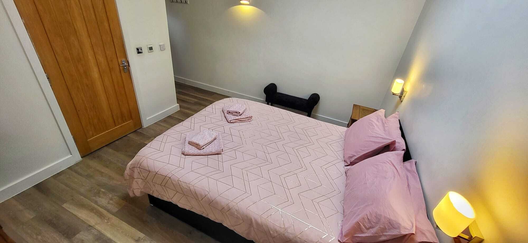 A bedroom with a bed, pillows, a nightstand, and a wall-mounted lamp.