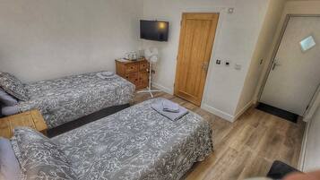 A bedroom with two beds, a TV, a fan, and a wardrobe.