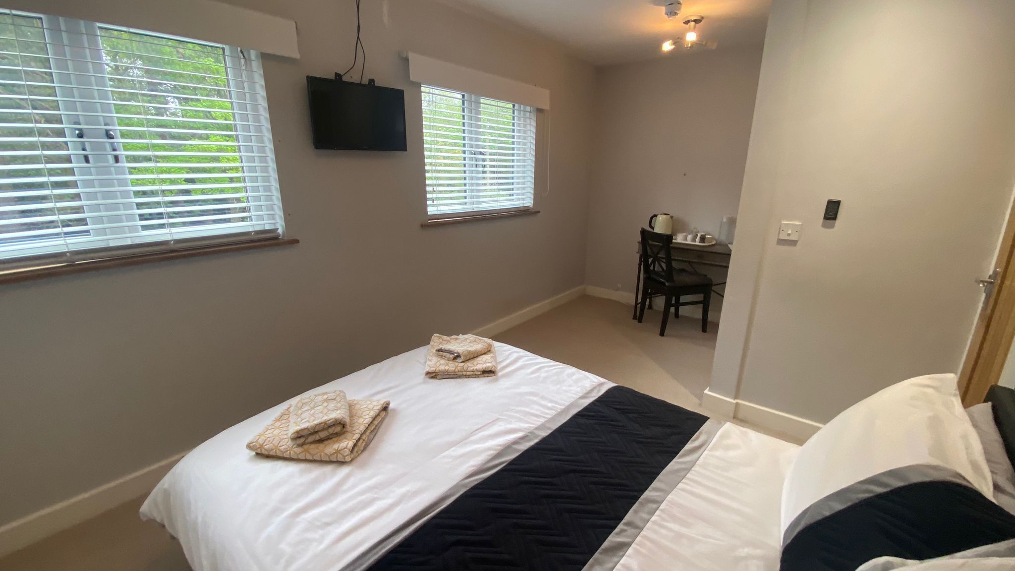 A bedroom with a bed, two windows, a desk, and a chair.