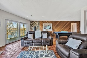 A modern living room with a brown leather sofa, a pool table, and a stone wall.