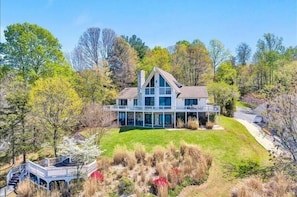 A large, modern two-story house with a wrap-around porch, surrounded by a well-maintained lawn and trees.