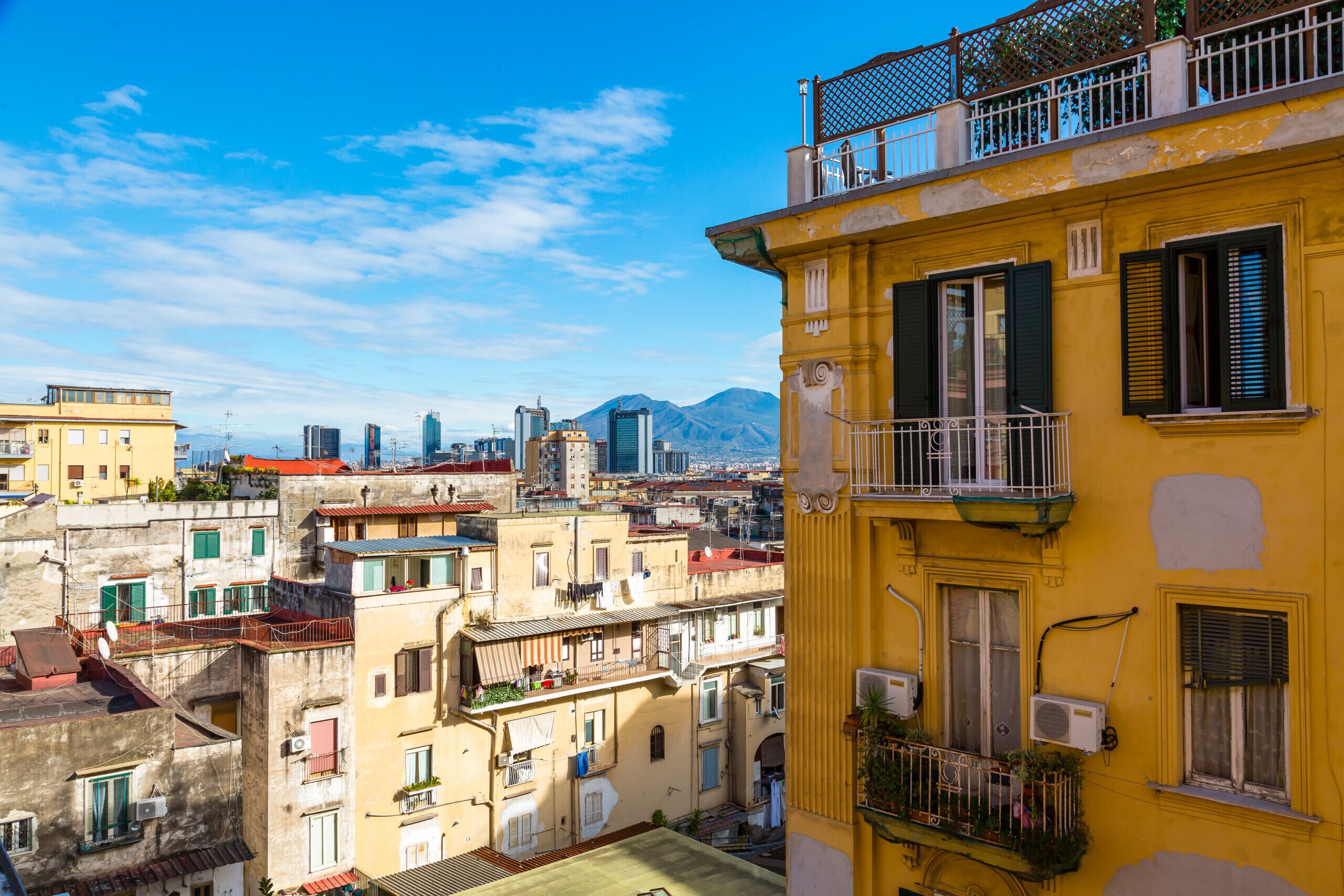 A yellow building with balconies, a cityscape in the background, and a mountain range.